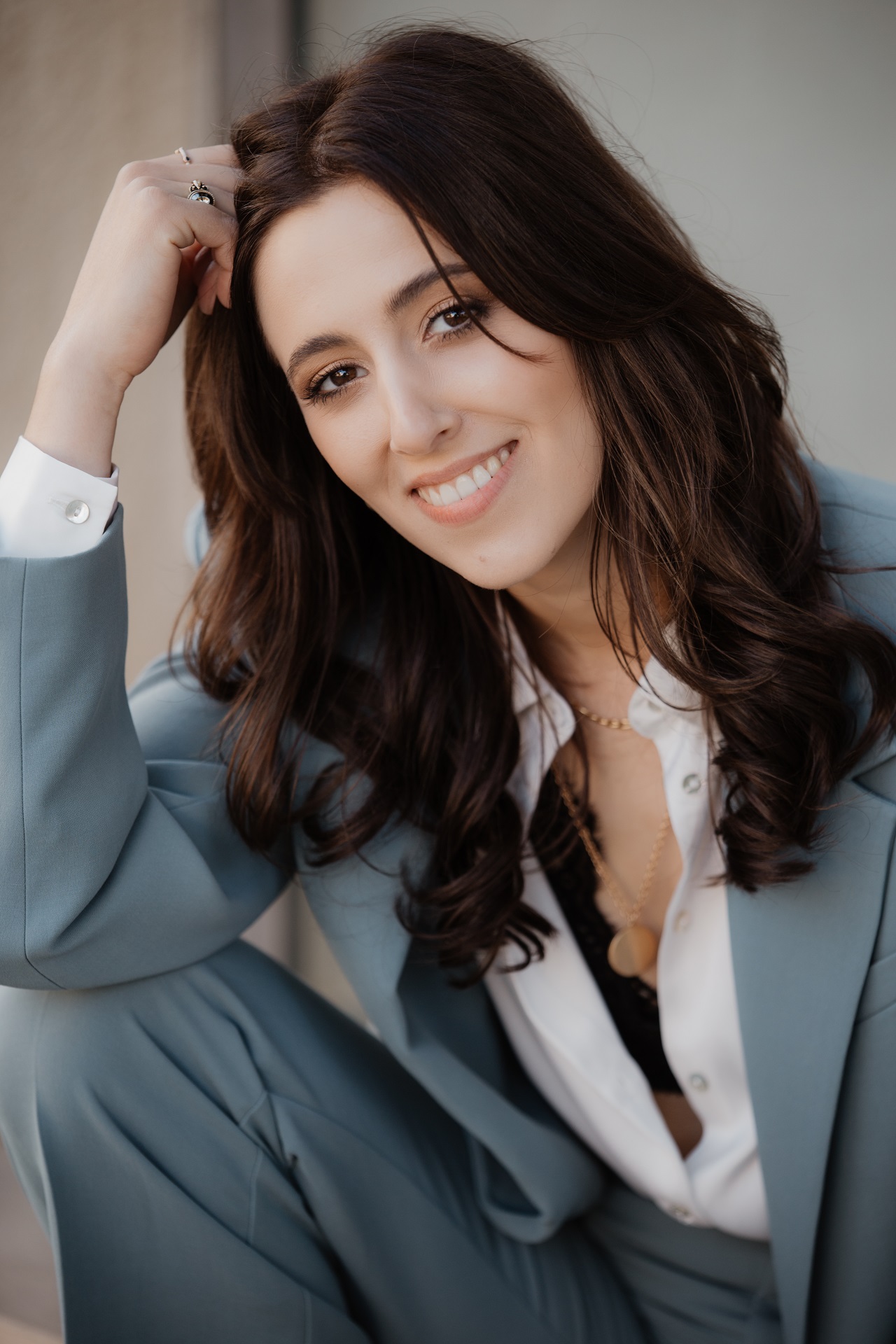 Picture of Stefanie Mayer, sitting with a light blue suit and a white blouse on the ground, kneeling and putting her arm on her knee